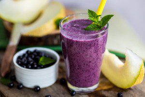 Blueberry smoothie in a glass with a straw and sprig of mint, ov