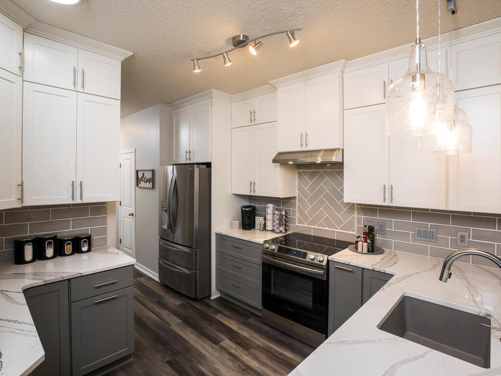 Two Toned Cabinets In Modern Kitchen. White cabinets up top dark grey cabinets with stainless steel hardware. White and grey marbled countertops. Grey Subway Tile Backsplash.