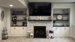 Family Room With Stone Fireplace. Modern white cabinets with black hardware and dark free standing shelves.